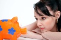 Young woman with head resting on arms, staring at a piggy bank.